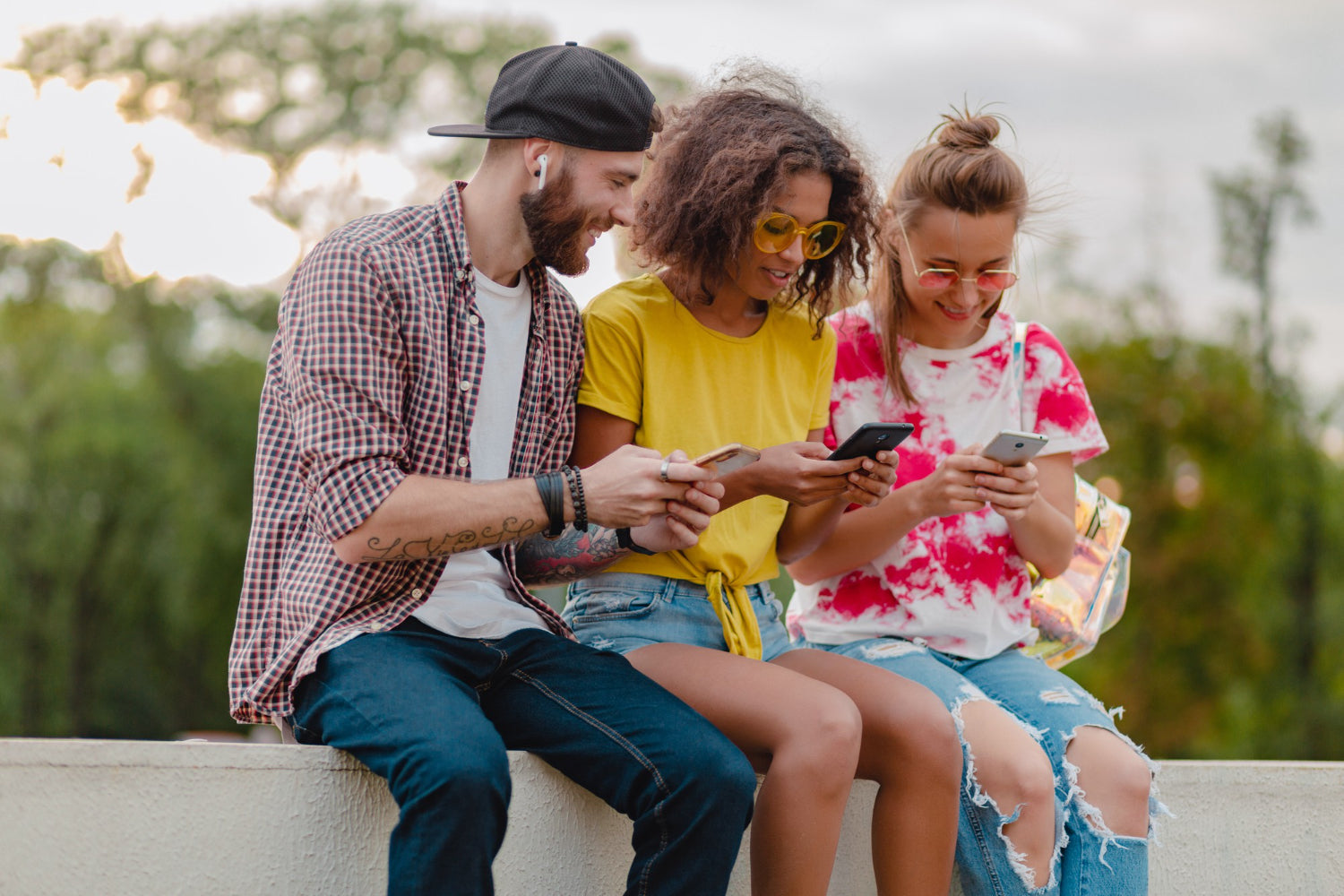 Three friends sitting outdoors, looking at their phones.