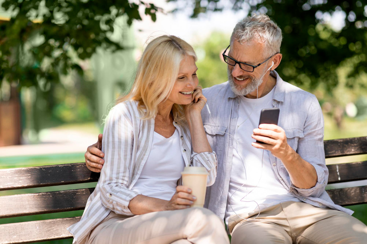 Man and woman sitting on a park bench, looking at a phone together.