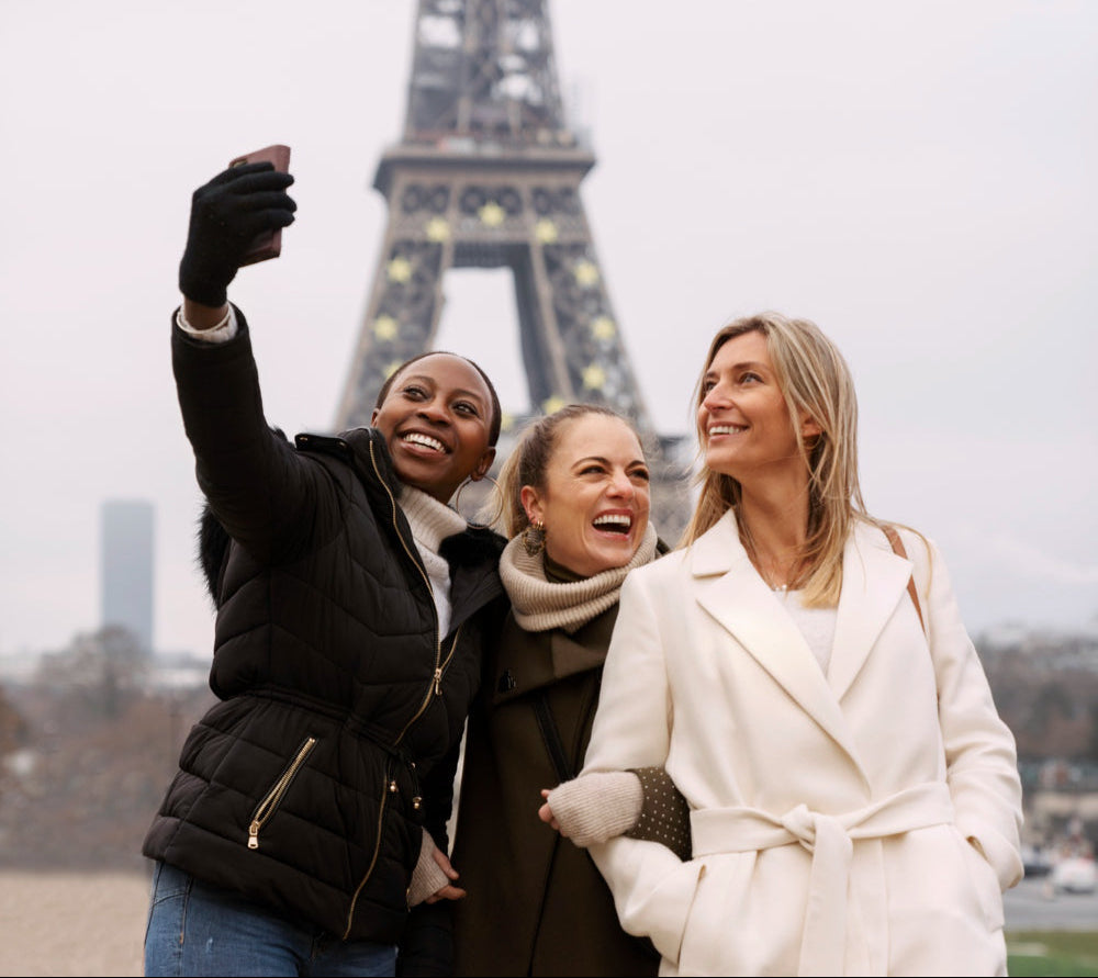 Three women taking a selfie in front of the Eiffel Tower on a cloudy day.